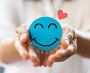 Smiling blue stress ball with heart in hands, a concept image for what is emotional health.